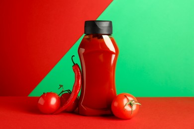 Photo of Bottle of ketchup, tomatoes and chili pepper on color background