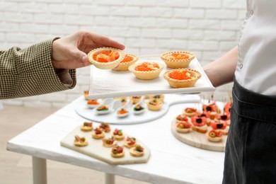 Photo of Woman taking tasty canape from waiter with board indoors, closeup