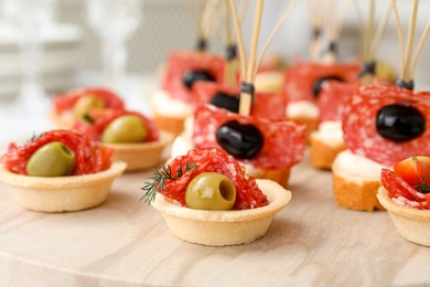 Photo of Many different tasty canapes on wooden board, closeup