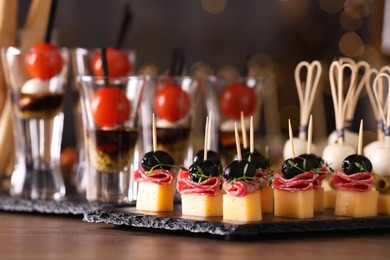 Photo of Many different tasty canapes on wooden table against blurred lights, closeup