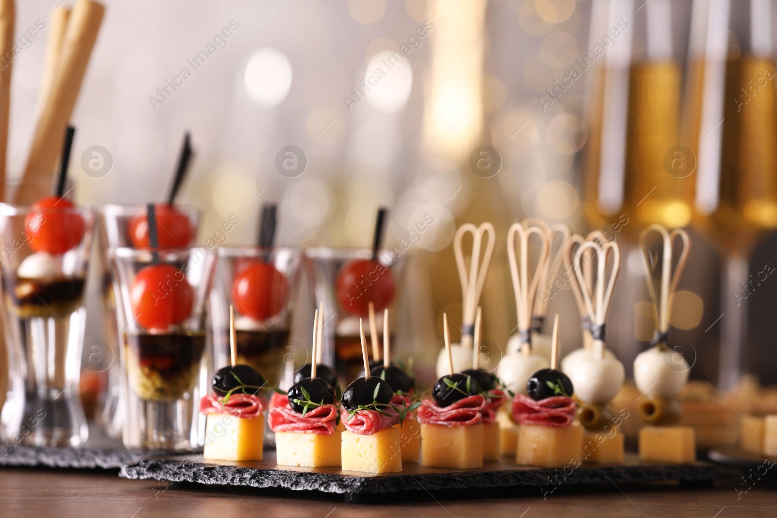 Photo of Many different tasty canapes on wooden table against blurred lights, closeup