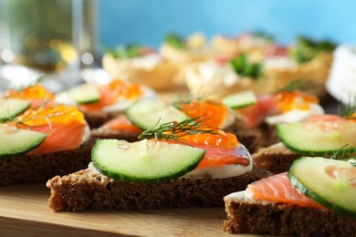 Photo of Tasty canapes with salmon and cucumber on wooden board, closeup