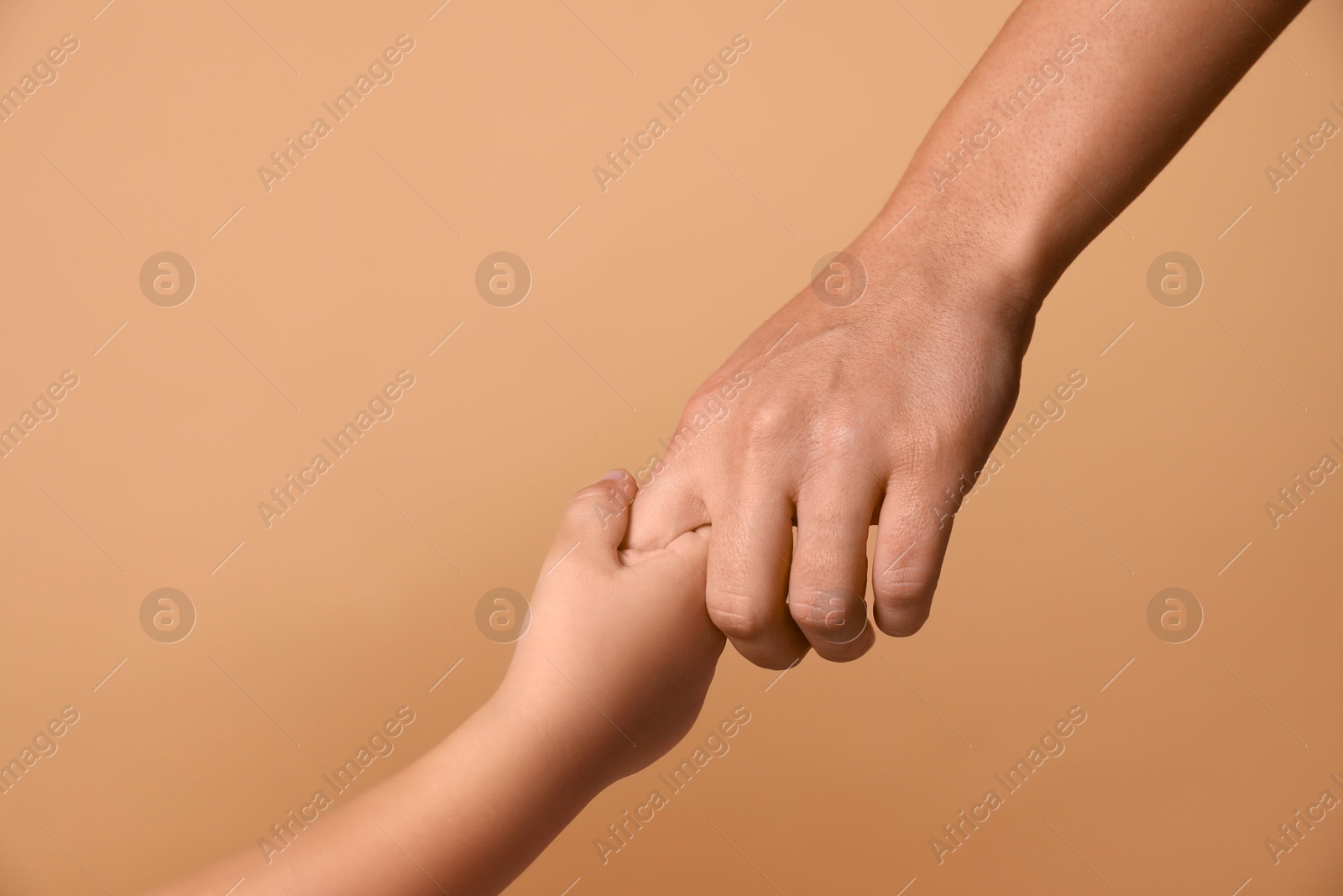 Photo of Mother and child holding hands on beige background, closeup