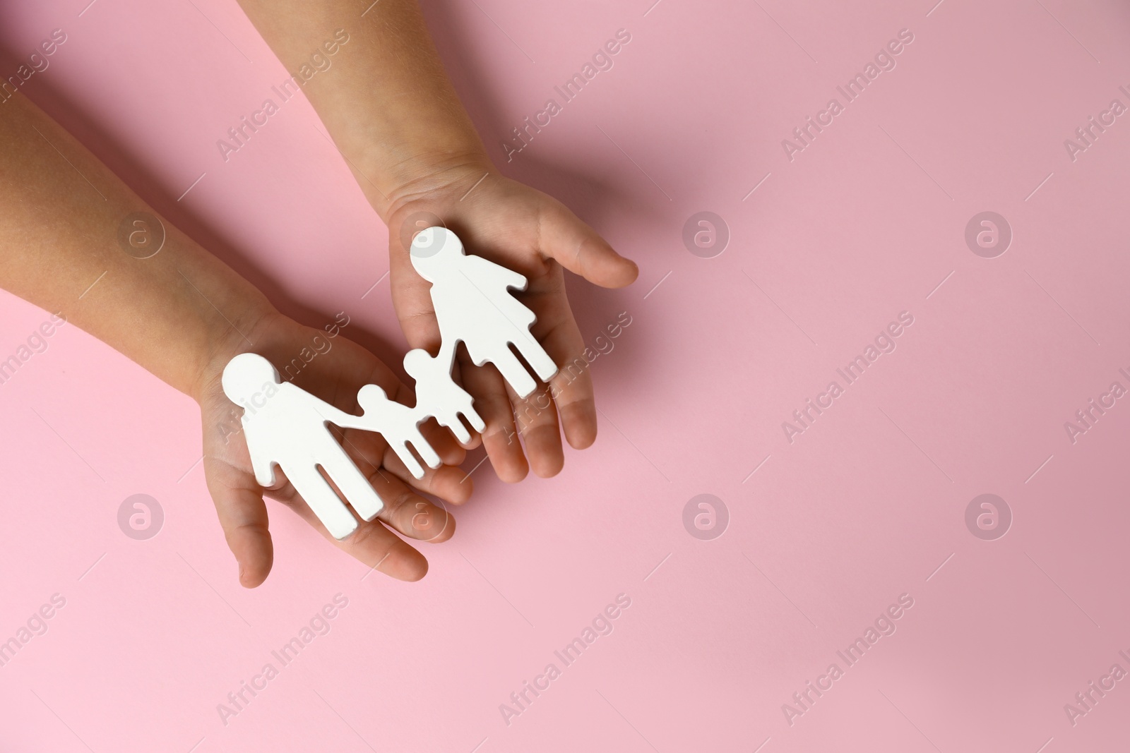 Photo of Child holding figure of family on light pink background, top view. Space for text