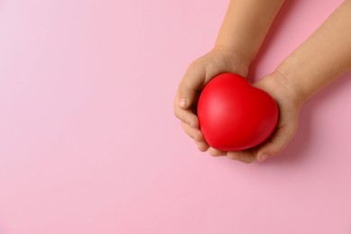 Photo of Child holding decorative red heart on light pink background, top view. Space for text