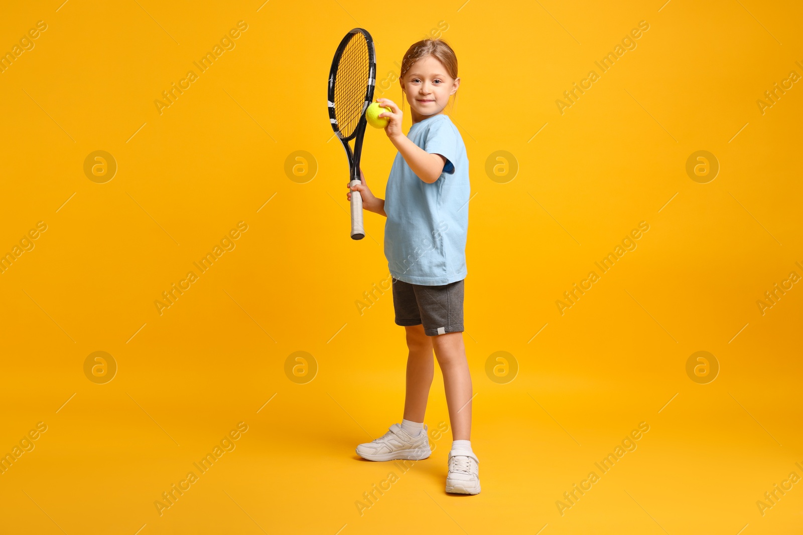 Photo of Cute little girl with tennis racket and ball on pink background