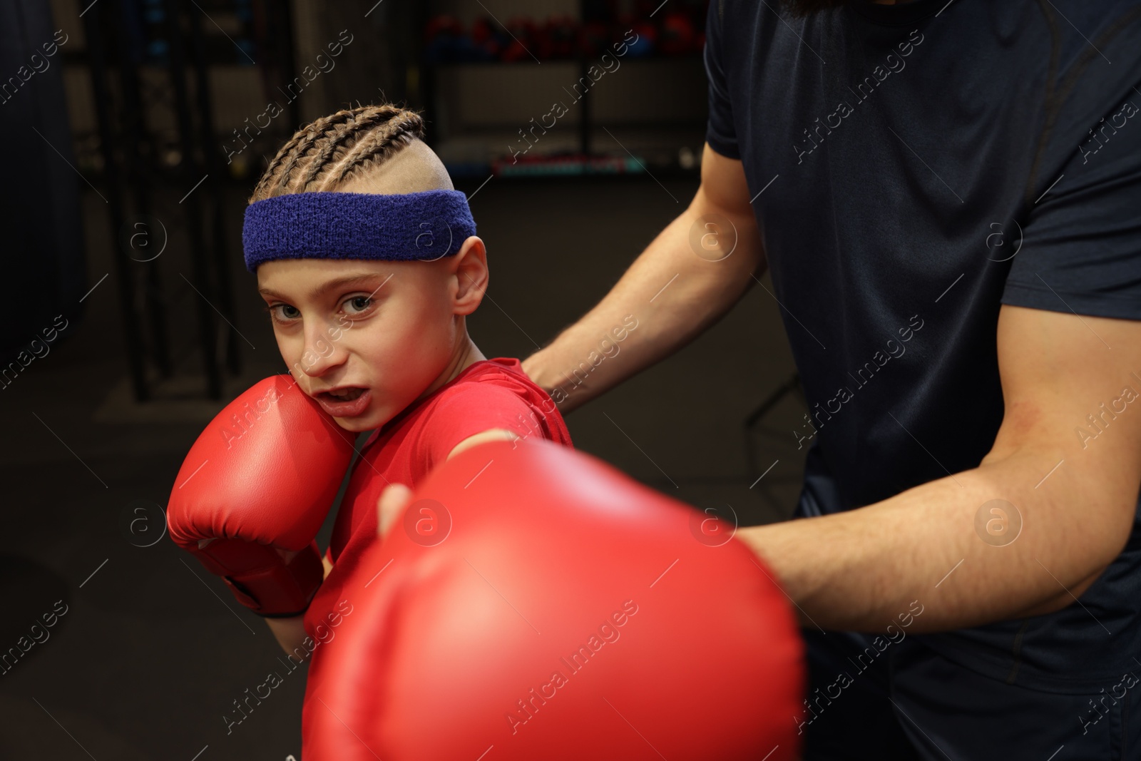 Photo of Boy in protective gloves with his boxing coach at training center