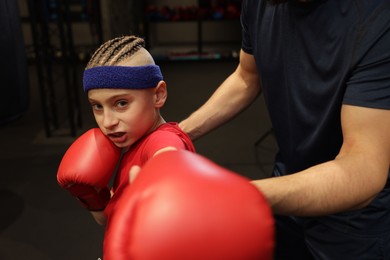 Photo of Boy in protective gloves with his boxing coach at training center