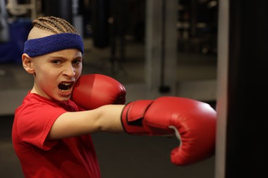 Photo of Boy in protective gloves exercising with punching bag during boxing practice at sport center