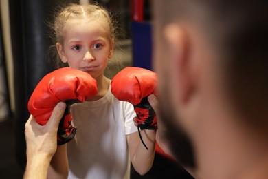 Photo of Girl in protective gloves having boxing practice with her coach at training center