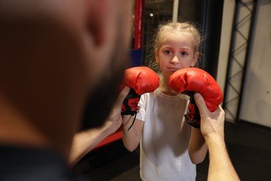 Photo of Girl in protective gloves having boxing practice with her coach at training center