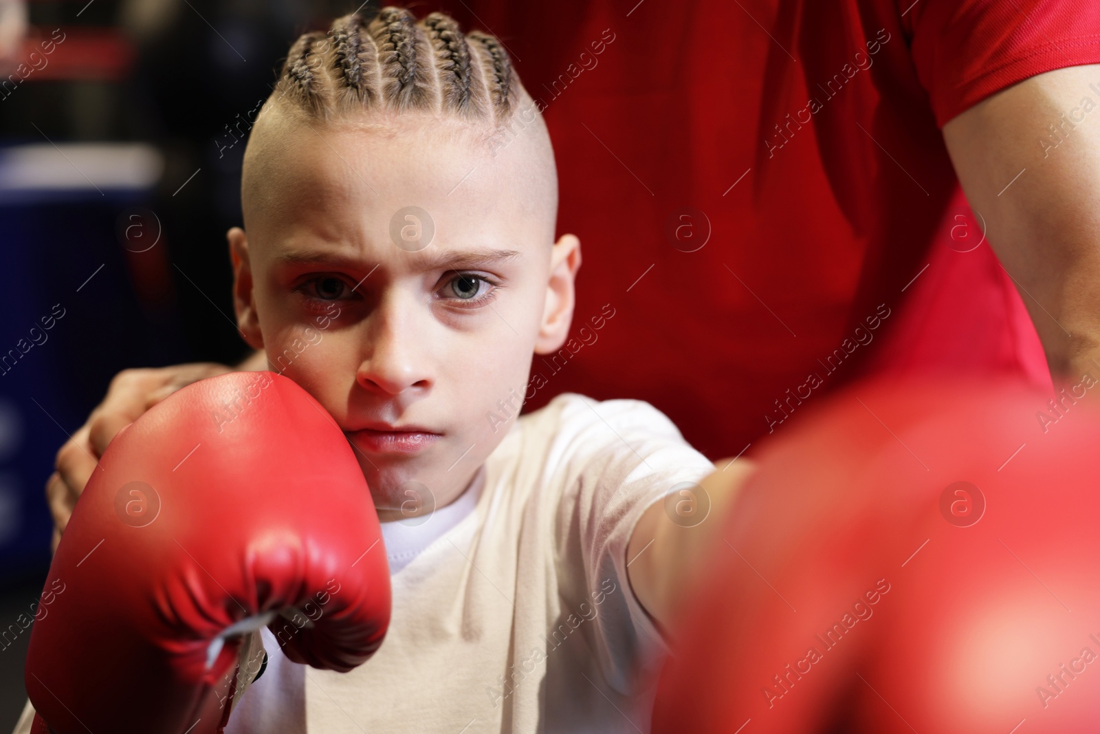 Photo of Boy in protective gloves with his boxing coach at training center