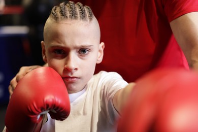 Boy in protective gloves with his boxing coach at training center