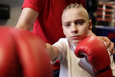 Photo of Boy in protective gloves with his boxing coach at training center