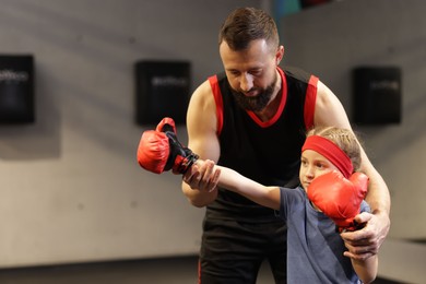 Photo of Girl in protective gloves having boxing practice with her coach at training center. Space for text