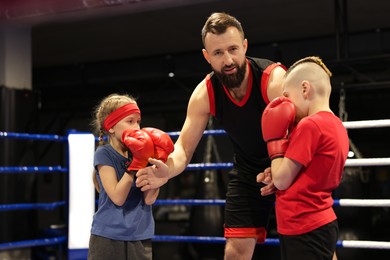 Photo of Children practicing fight on boxing ring under their coach supervision