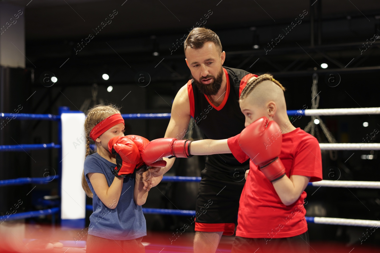 Photo of Children practicing fight on boxing ring under their coach supervision