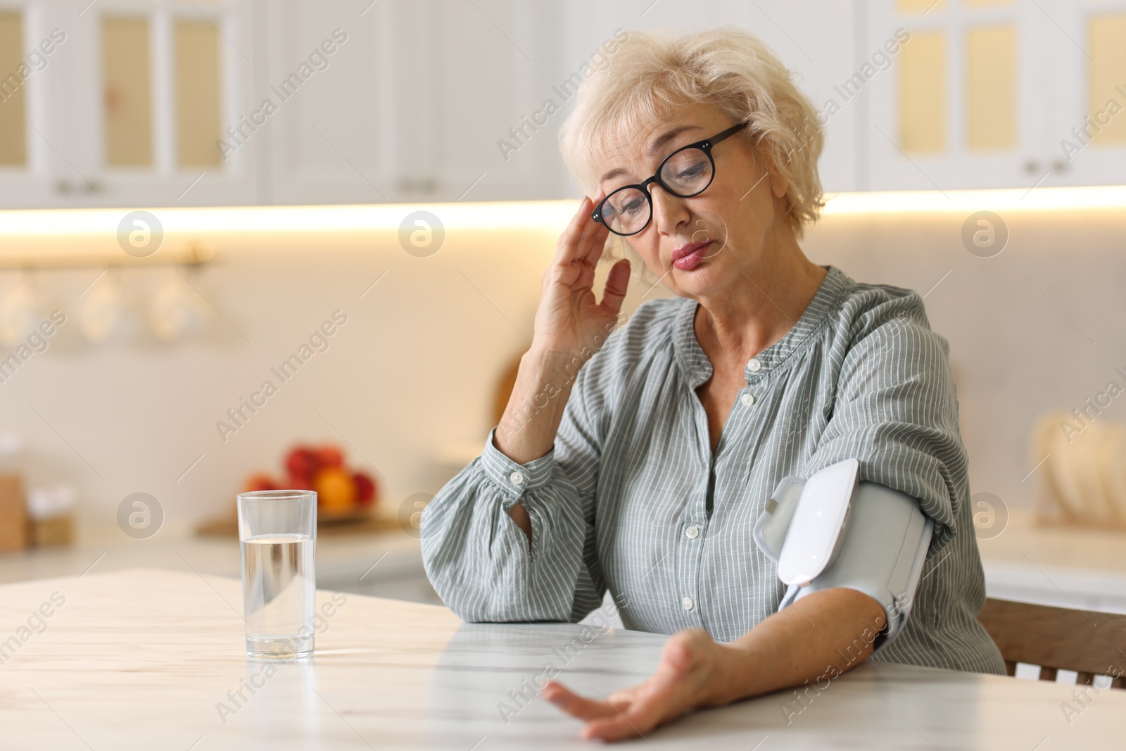 Photo of Senior woman measuring blood pressure at table in kitchen. Space for text