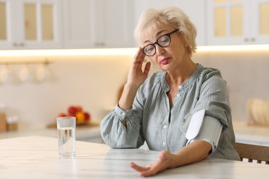 Photo of Senior woman measuring blood pressure at table in kitchen. Space for text