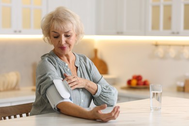 Photo of Senior woman measuring blood pressure at table in kitchen. Space for text