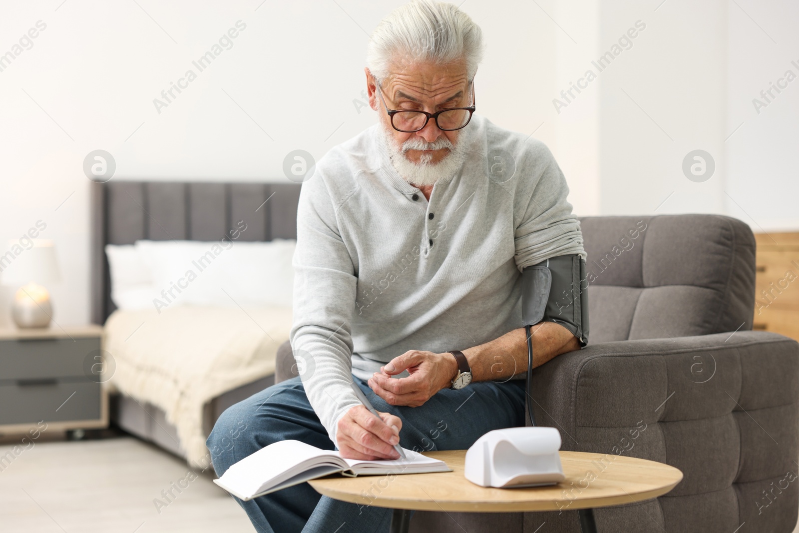 Photo of Senior man writing results of blood pressure measurement at home