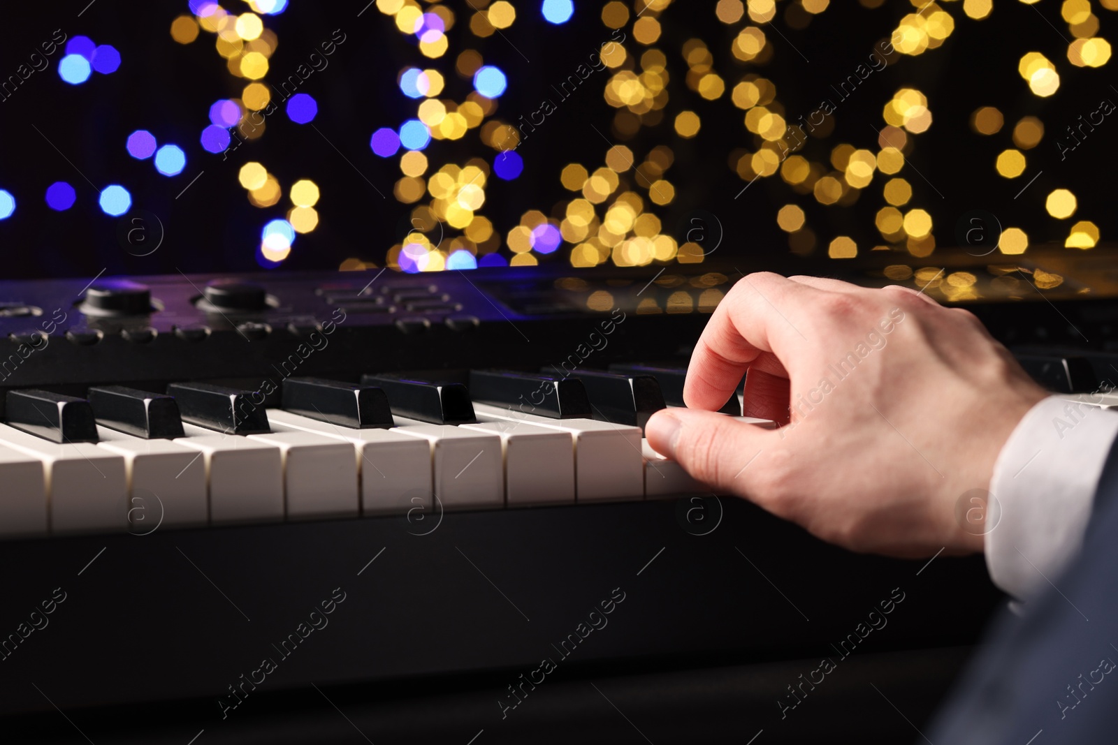 Photo of Man playing piano against blurred lights, closeup. Bokeh effect