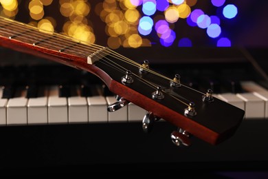 Photo of Guitar on piano against blurred lights, closeup. Bokeh effect