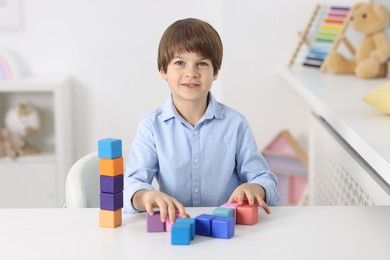 Photo of Happy boy with tower of colorful cubes at table indoors