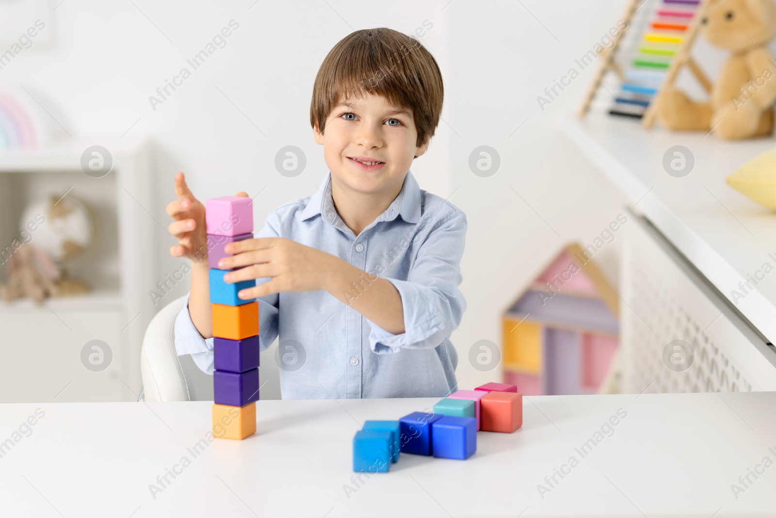 Photo of Happy boy building tower of colorful cubes at table indoors