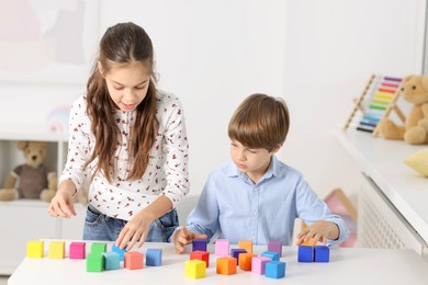 Children playing with colorful cubes at table indoors