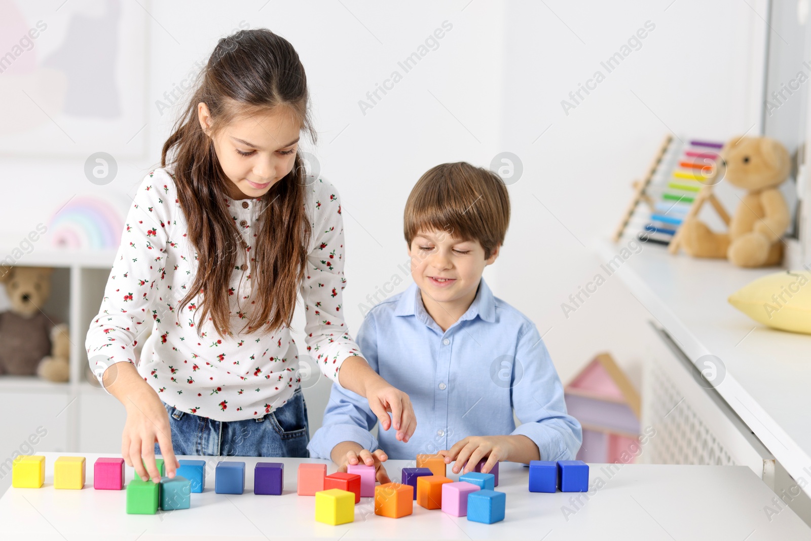 Photo of Children playing with colorful cubes at table indoors