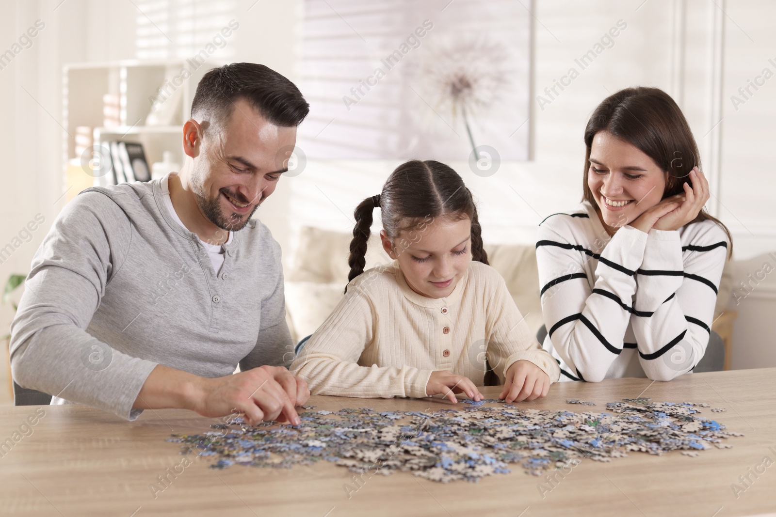 Photo of Happy parents and their daughter solving puzzle together at wooden table indoors