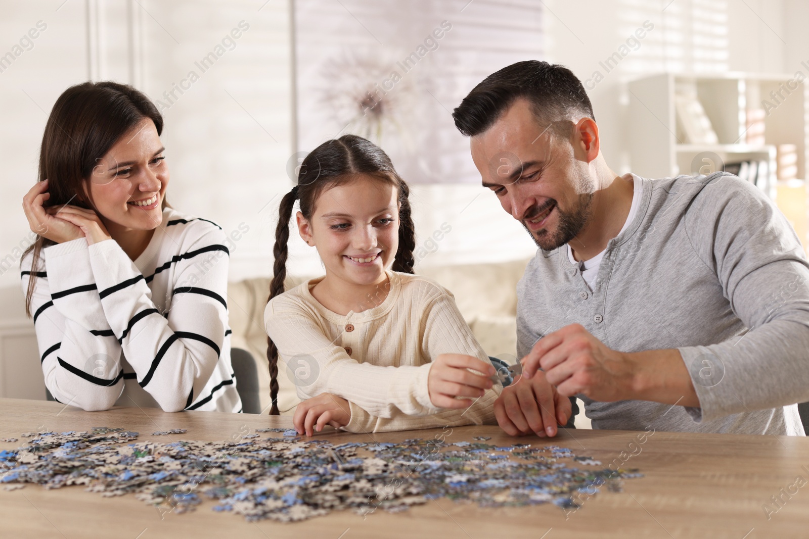 Photo of Happy parents and their daughter solving puzzle together at wooden table indoors