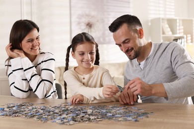 Photo of Happy parents and their daughter solving puzzle together at wooden table indoors