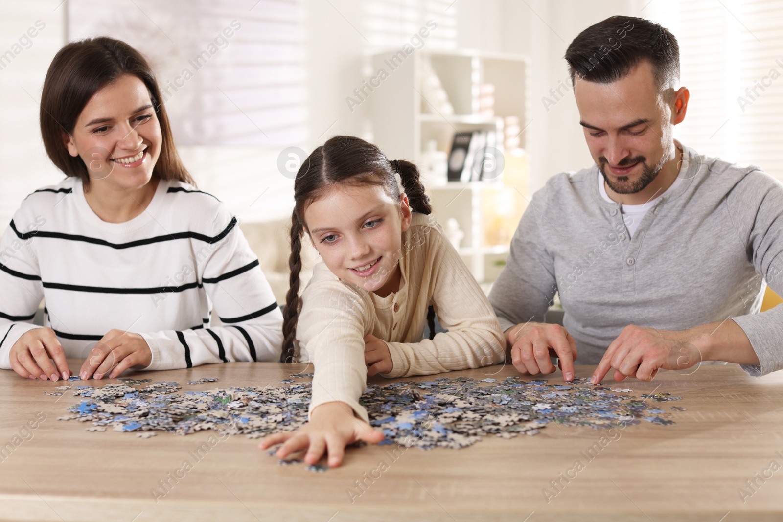 Photo of Happy parents and their daughter solving puzzle together at wooden table indoors