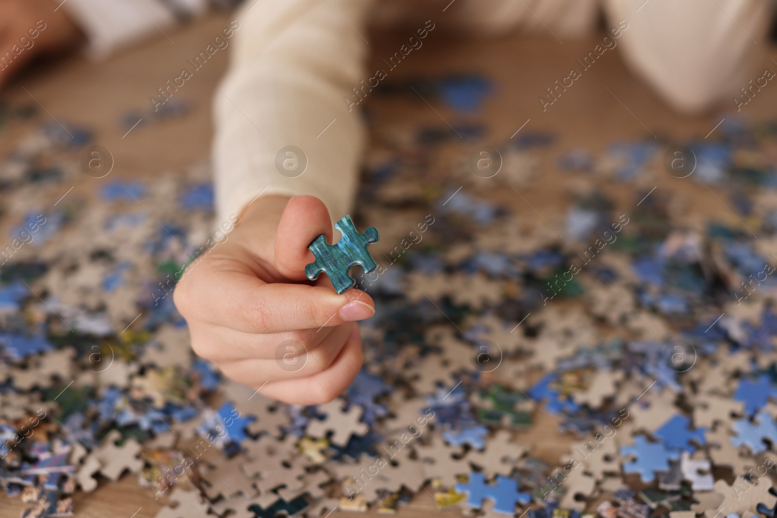 Photo of Girl solving puzzle at wooden table, closeup