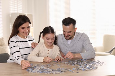 Photo of Happy parents and their daughter solving puzzle together at wooden table indoors