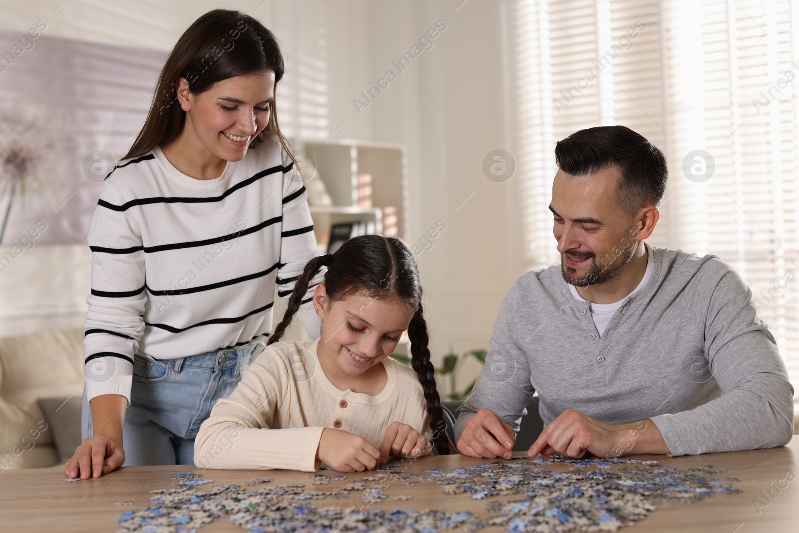 Photo of Happy parents and their daughter solving puzzle together at wooden table indoors