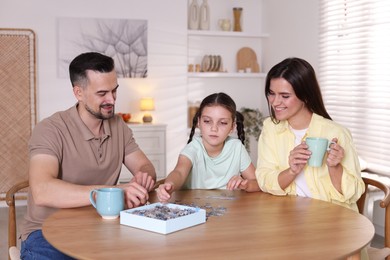 Photo of Happy parents and their daughter solving puzzle together at wooden table indoors