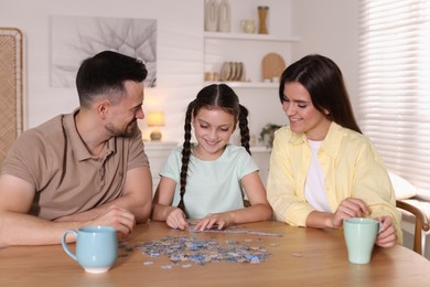 Photo of Happy parents and their daughter solving puzzle together at wooden table indoors