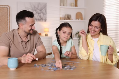 Photo of Happy parents and their daughter solving puzzle together at wooden table indoors