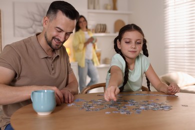 Photo of Happy father and his daughter solving puzzle together at wooden table indoors, selective focus