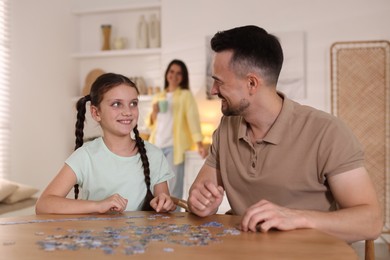 Photo of Happy father and his daughter solving puzzle together at wooden table indoors, selective focus