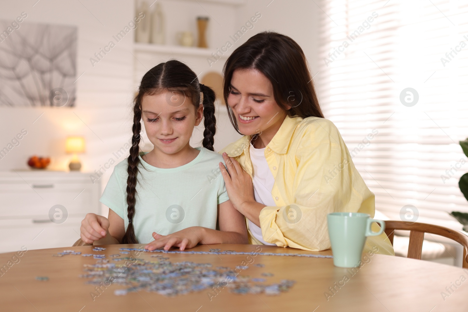 Photo of Happy mother and her daughter solving puzzle together at wooden table indoors