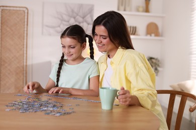 Photo of Happy mother and her daughter solving puzzle together at wooden table indoors