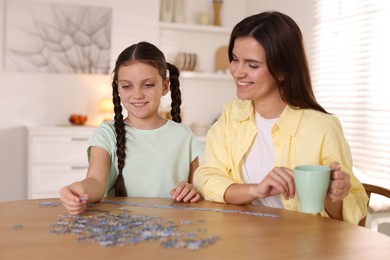 Photo of Happy mother and her daughter solving puzzle together at wooden table indoors