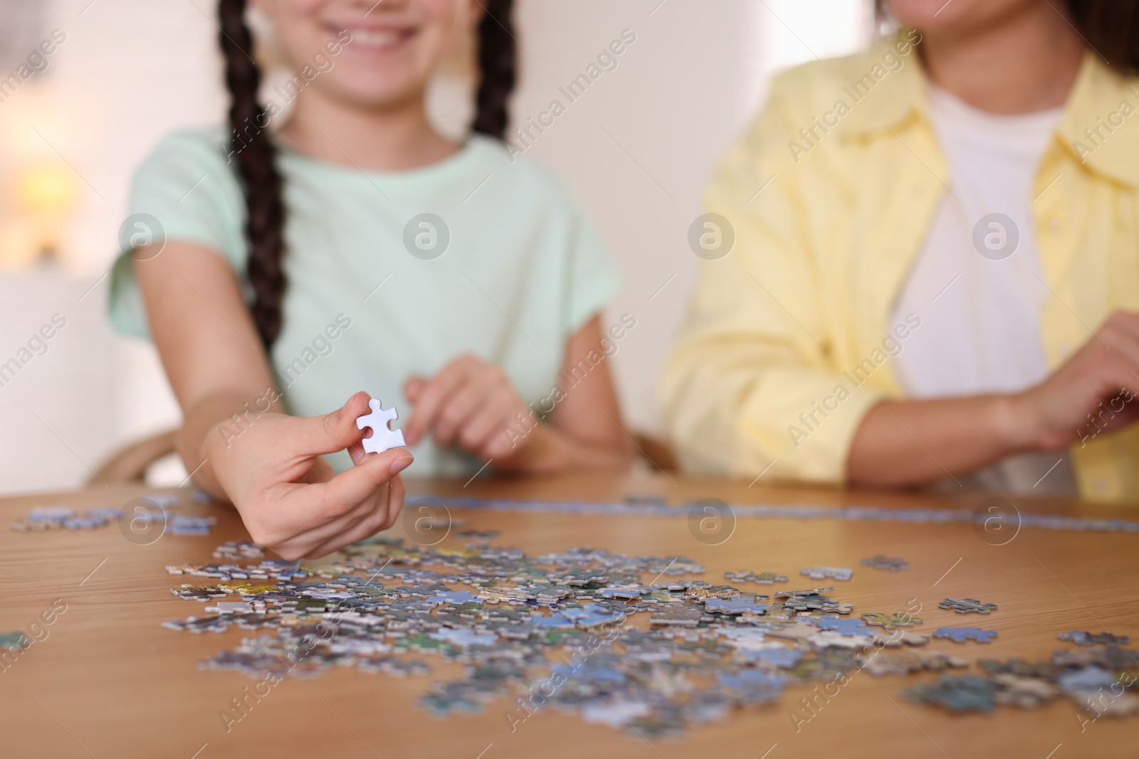 Photo of Mother and her daughter solving puzzle together at wooden table indoors, closeup