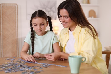 Photo of Happy mother and her daughter solving puzzle together at wooden table indoors