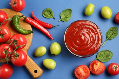 Photo of Tasty ketchup and vegetables on blue background, flat lay