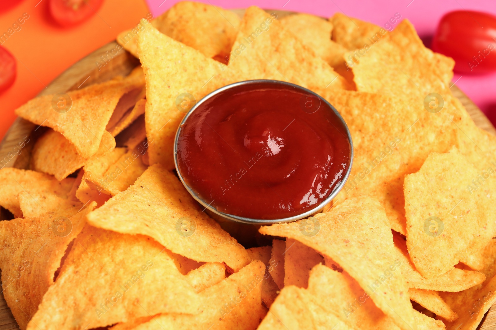 Photo of Tasty ketchup and nachos on color background, closeup